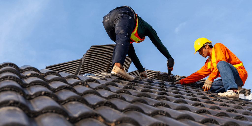 Roofer installing tiles on a pitched roof with scaffolding safely erected around the building.