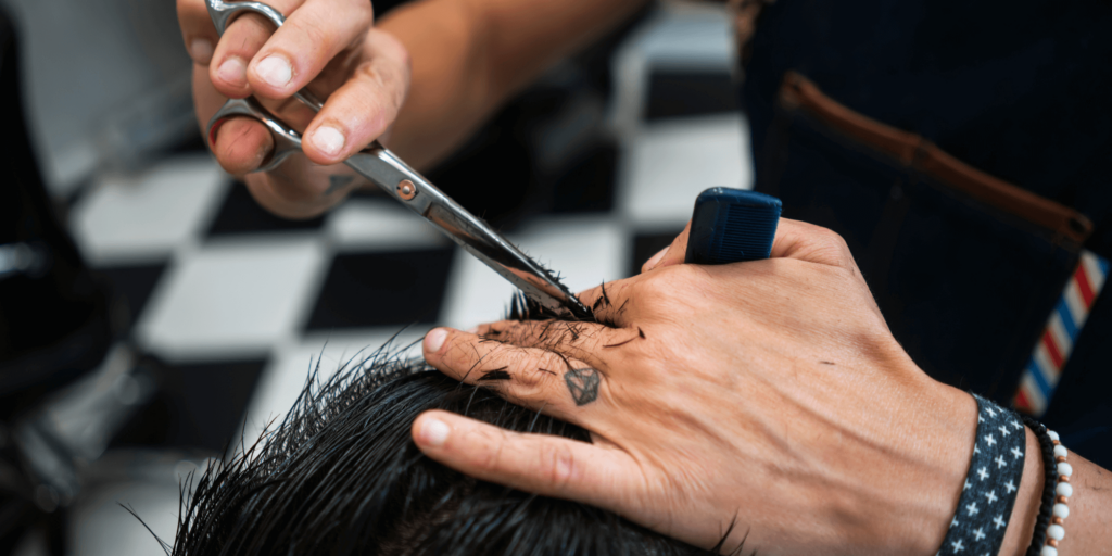 Smiling barber in an apron using clippers to cut a client’s hair in a modern, stylish barbershop.