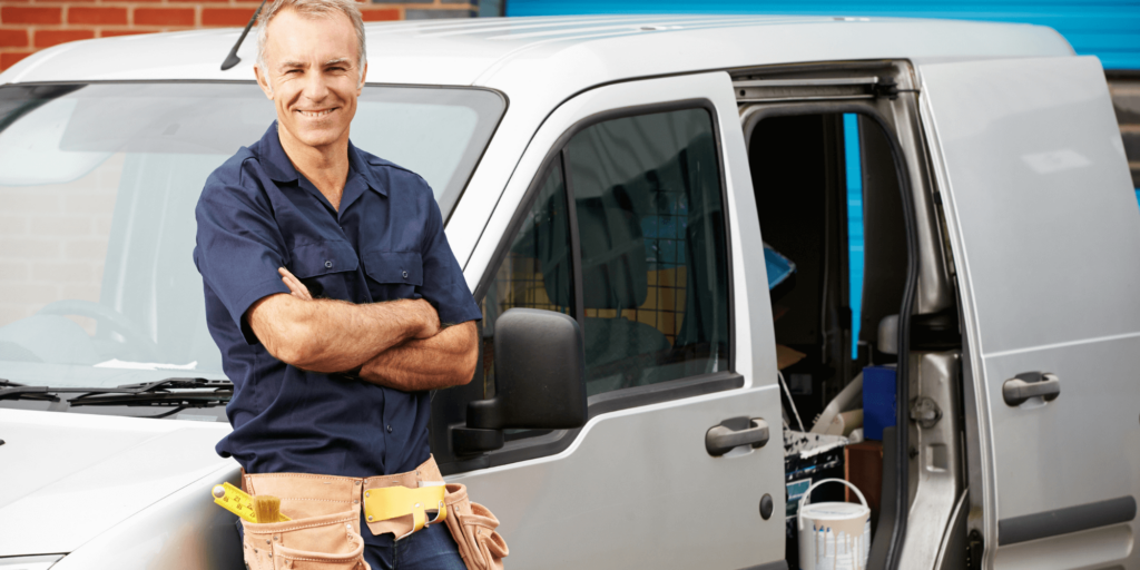 Self-employed tradesperson loading tools into a van outside a residential property.