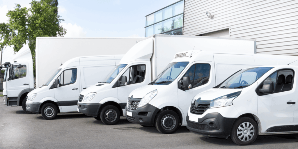 Line-up of white commercial vans and trucks parked outside a business premises in the UK, representing business vehicle insurance cover for fleets.